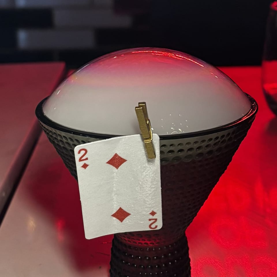 A cocktail in a textured glass with a smoke bubble on top, garnished with a playing card.