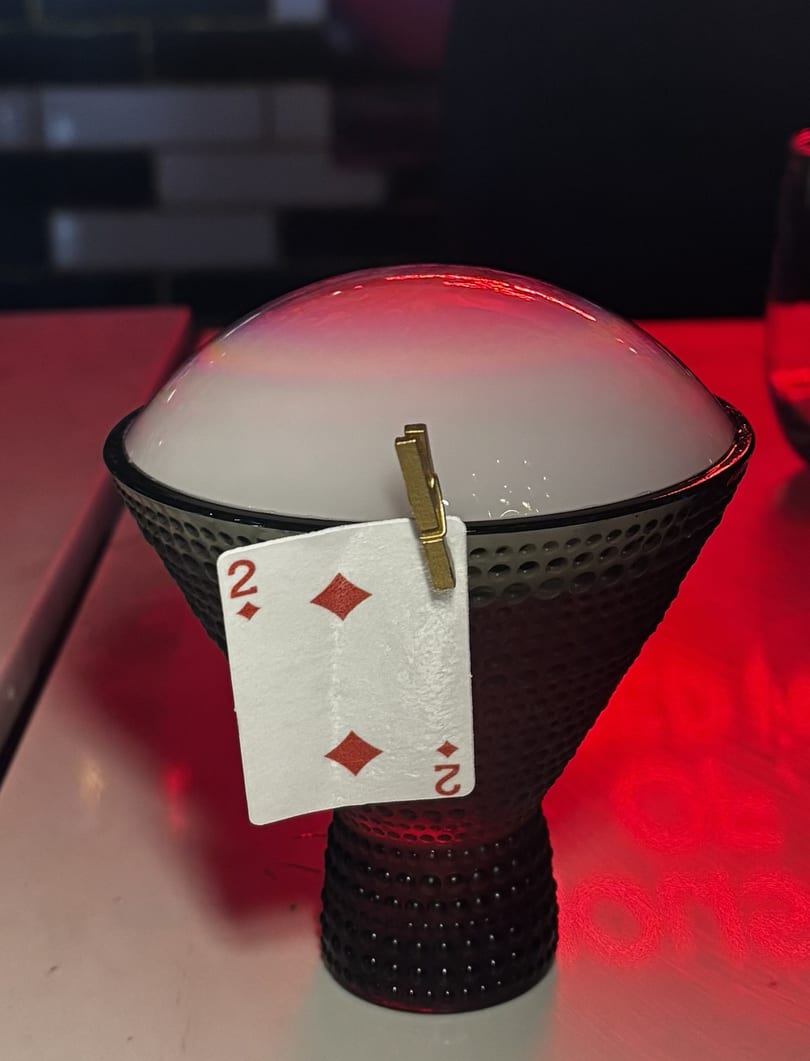 A cocktail in a textured glass with a smoke bubble on top, garnished with a playing card.
