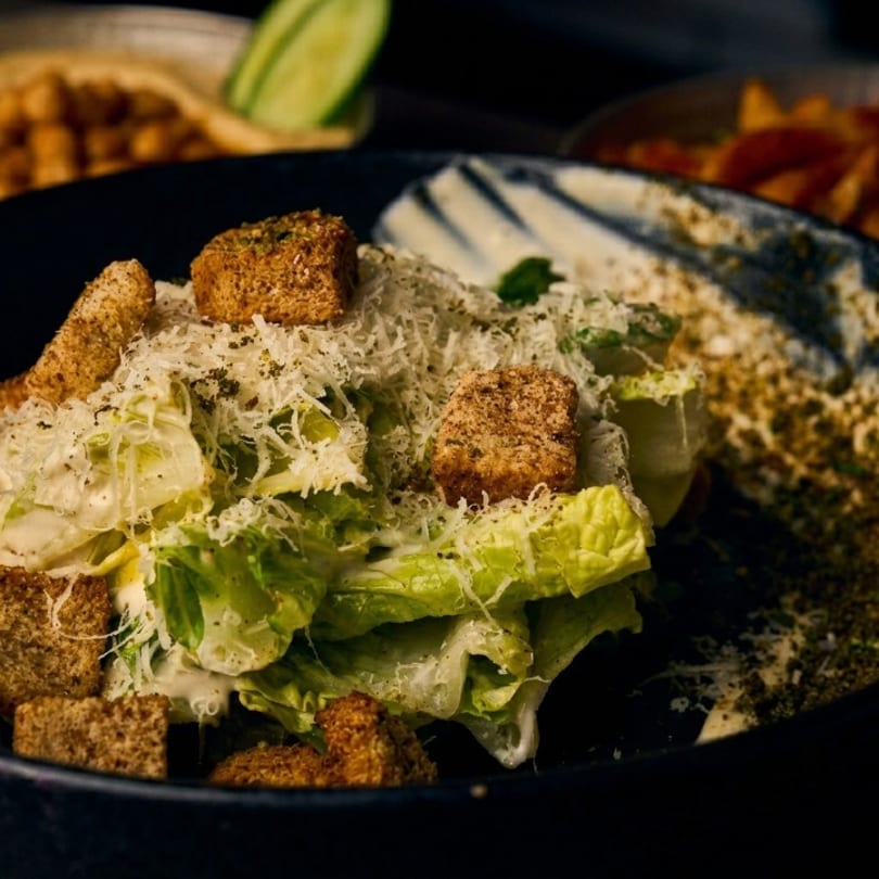 Close-up of a Caesar salad with croutons and grated cheese in a dark bowl.