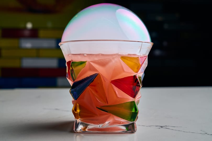 Pink cocktail in a colorful geometric glass, topped with a shimmering smoke bubble.