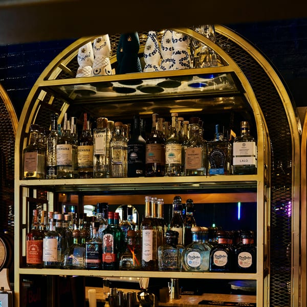 Well-stocked bar shelves with many tequila and mezcal bottles on golden arched racks.