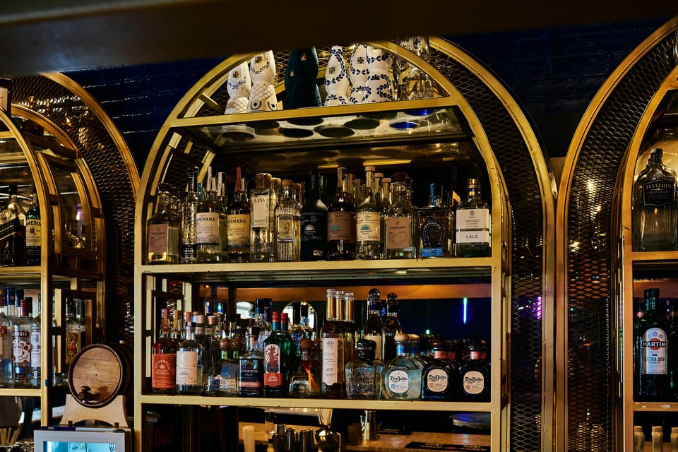 A well-stocked bar with numerous bottles of tequila and other spirits on golden arched shelves.