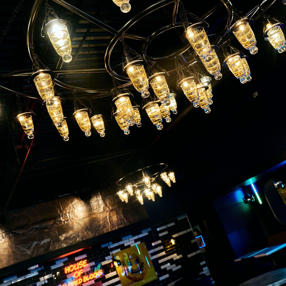 Dimly lit restaurant interior with numerous glowing spiral pendant lights, neon wall art, and dark seating.