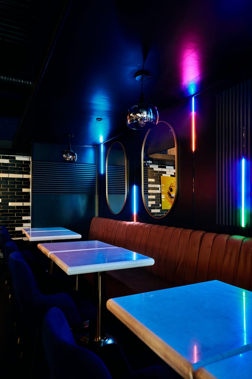 Vibrant restaurant interior with marble tables, velvet seating, and colorful neon strip lights.
