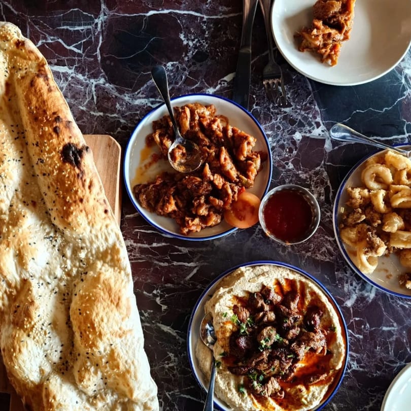 Overhead view of Mediterranean dishes including flatbread, hummus with meat, and fried calamari on a marble table.